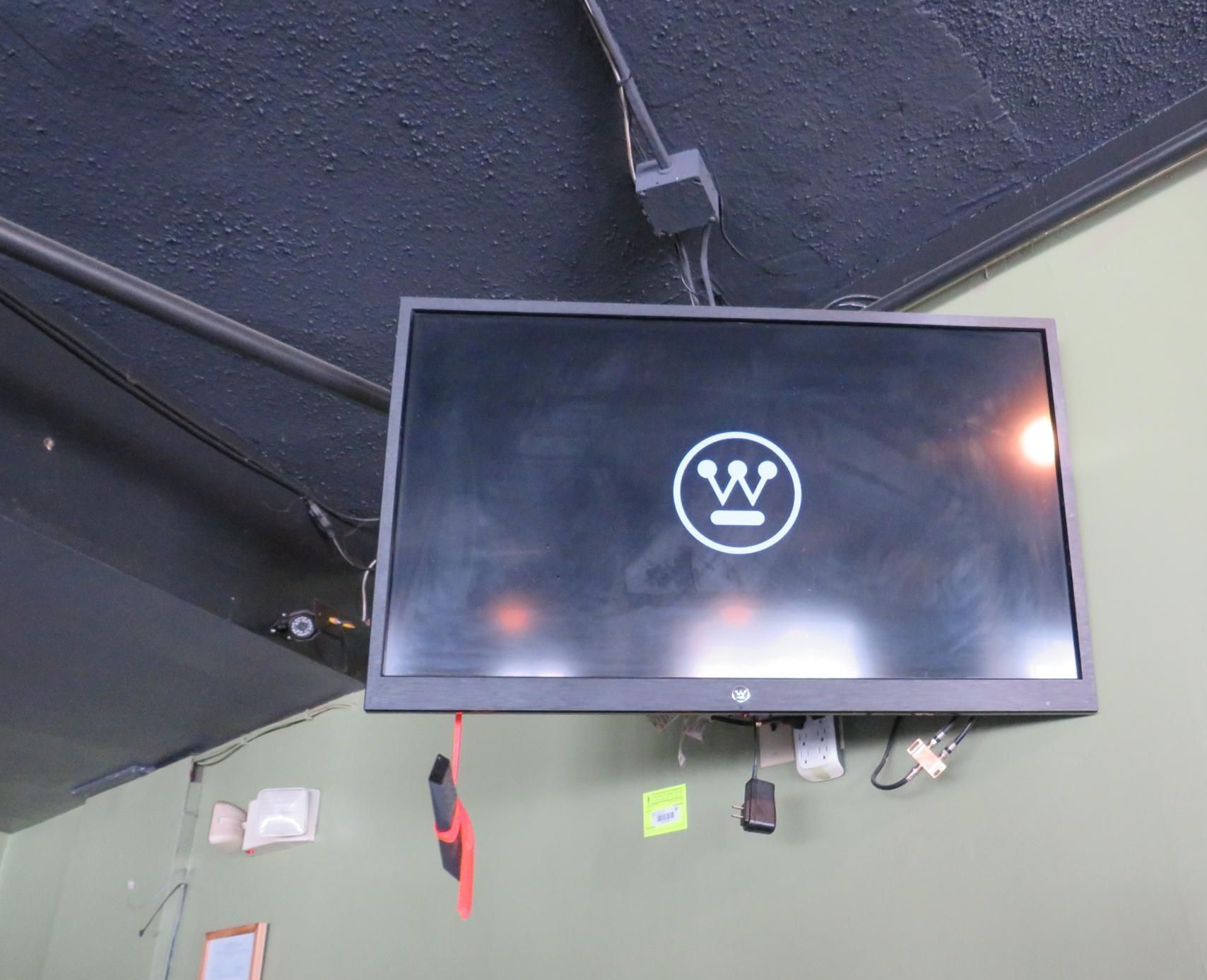 A wall-mounted TV with a circular logo, black screen, and visible cables.