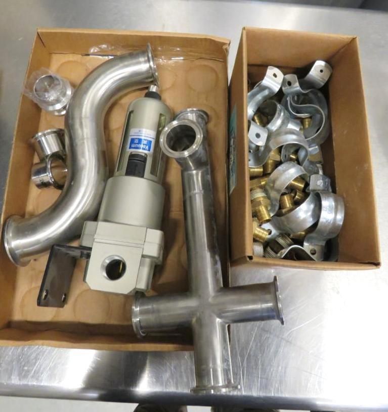 Two open boxes with stainless steel pipe fittings and clamps on a metal surface.