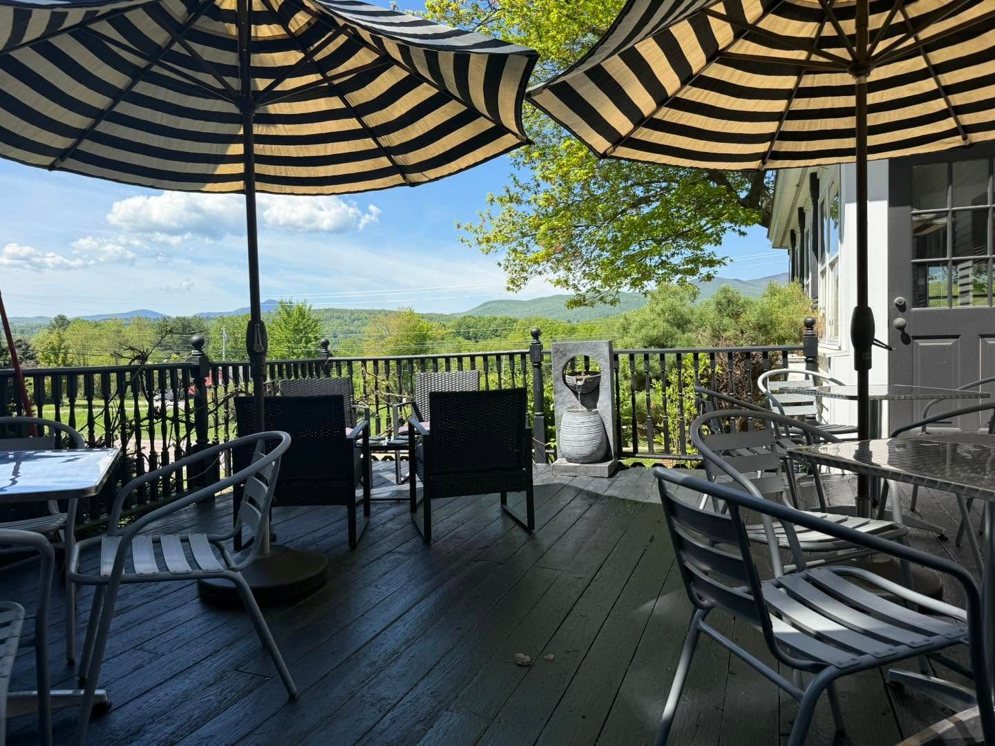 Patio with striped umbrellas, metal chairs, and a scenic view beyond a railing
