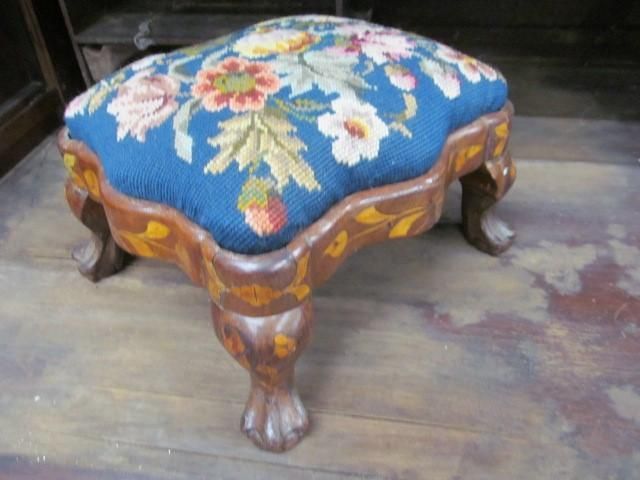 Small footstool with blue needlepoint floral design, wooden base, and ornate legs.