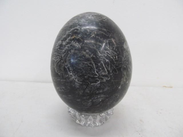 Black stone egg on a clear, faceted glass pedestal, set against a white backdrop.
