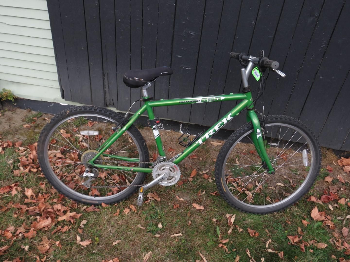 Green Trek mountain bike parked outside against a black wall.