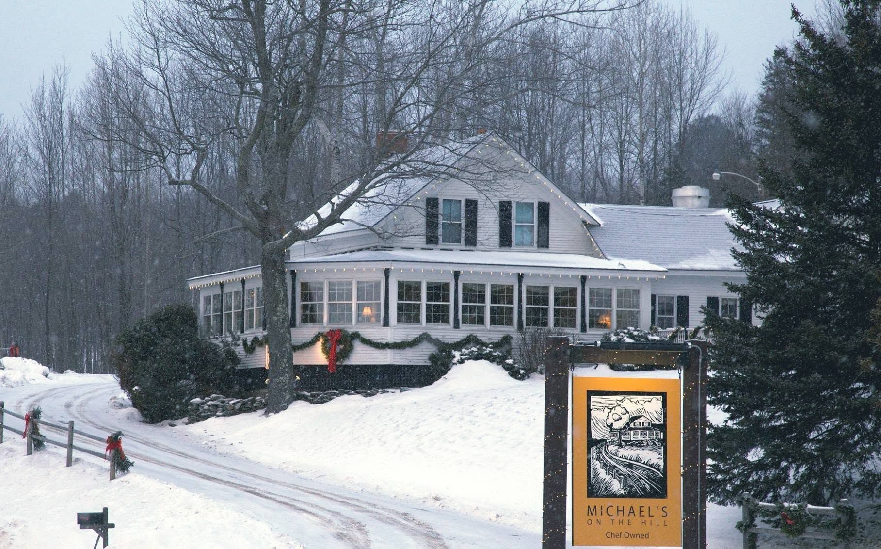 Snowy white house with porch and yellow sign beside a road in winter