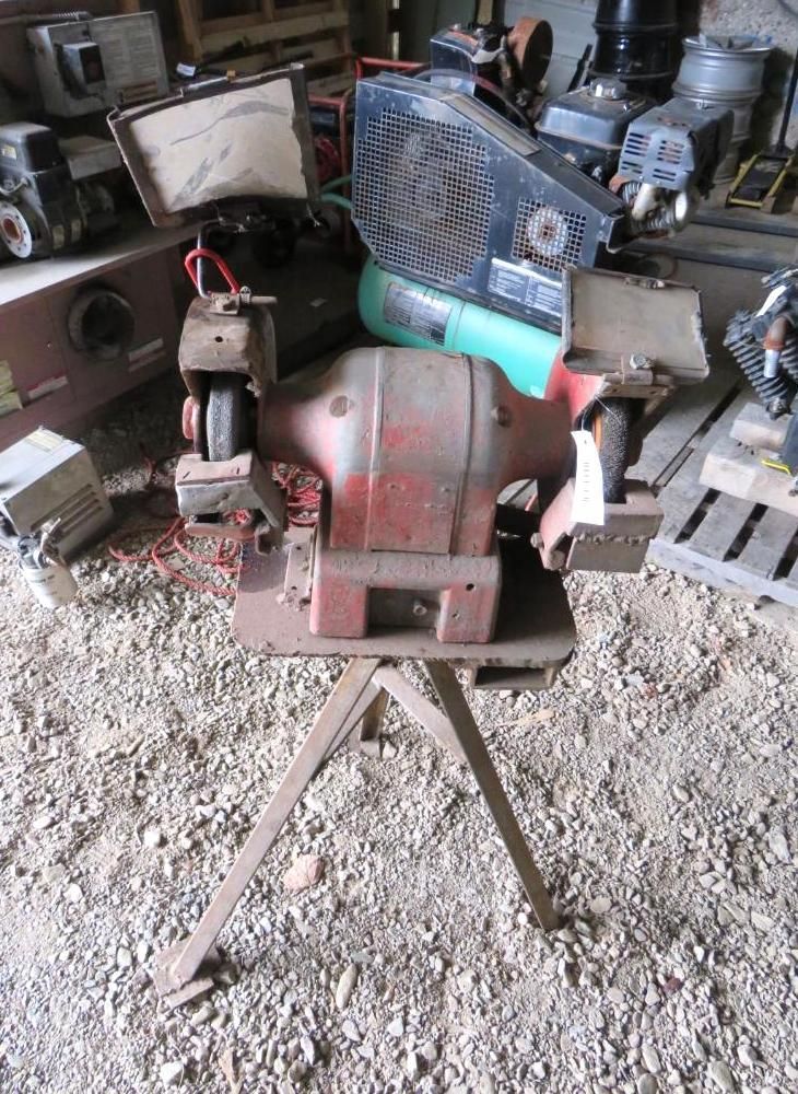 Red bench grinder on a metal stand in a workshop.