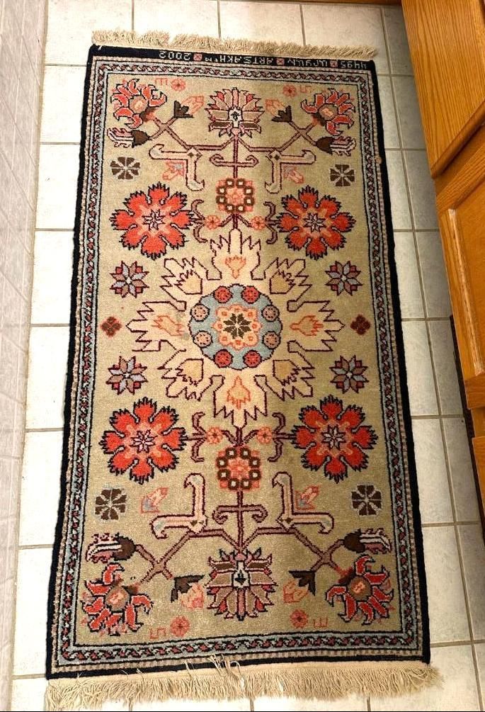 Rectangular rug with floral and geometric patterns, cream background, red and blue accents, black border, fringed ends.
