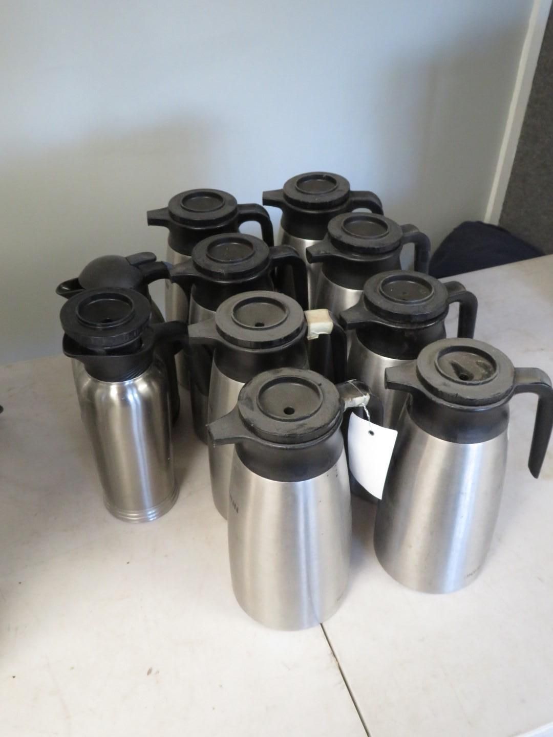 Silver insulated carafes with black lids and handles, grouped together on a white surface.