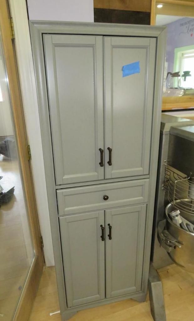 Tall gray storage cabinet with doors and drawer; black hardware.