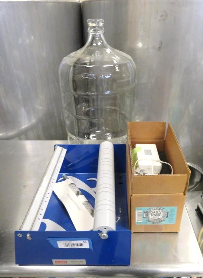 Large glass bottle, a blue box with components, and a brown box on a stainless steel surface.
