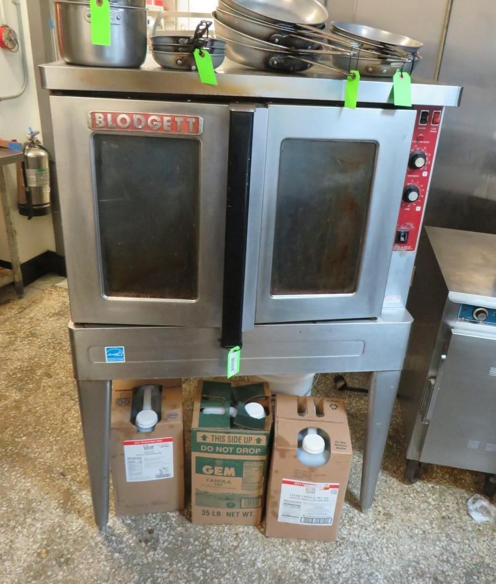 Commercial oven with two doors, stainless steel. Kitchen setting with supplies on shelves.