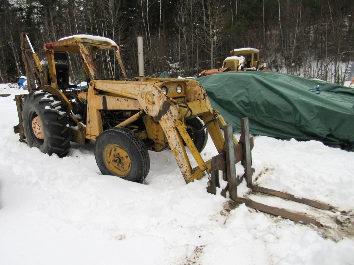 Yellow backhoe with front forks in snow.
