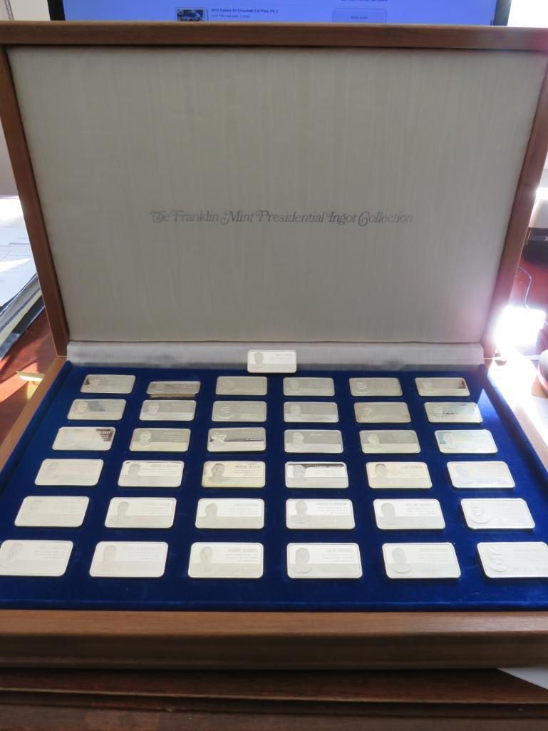 Wooden box open to reveal multiple rectangular silver bars arranged on a blue surface.