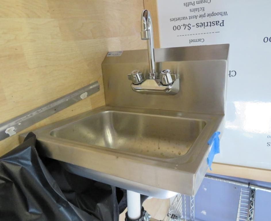 Stainless steel sink with faucet and backsplash mounted on a wall.