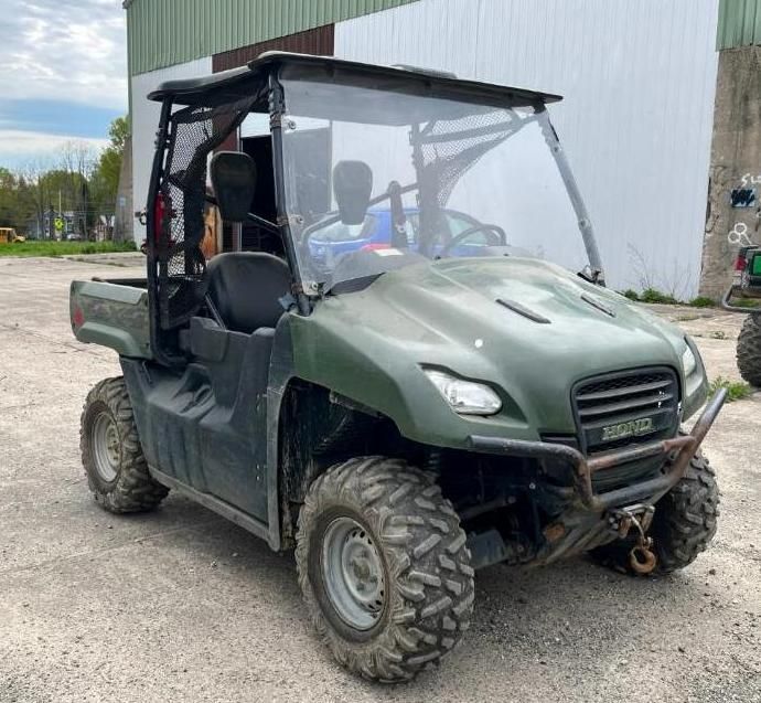 Green UTV with a windshield, roll cage, and off-road tires, parked on a gravel surface.