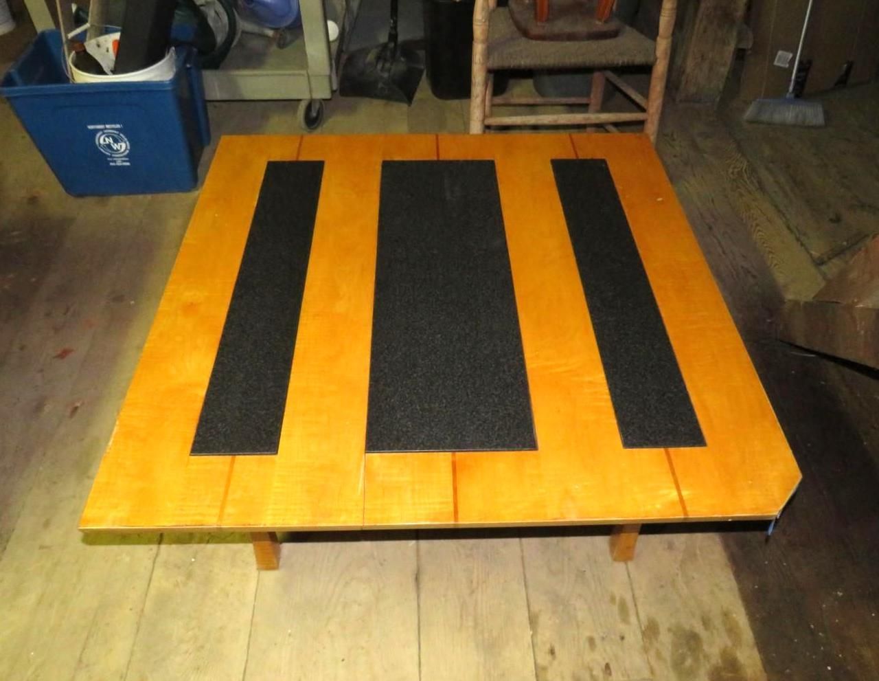 Wooden table with three black textured strips on a wood floor.