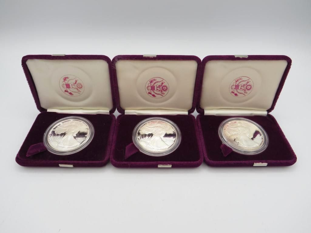 Three silver coins in open maroon velvet presentation boxes.