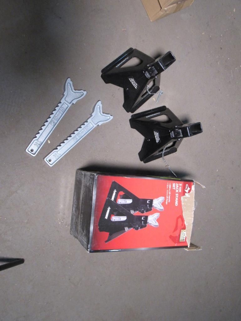 Black car jack stands, two wrenches, and a box on a concrete surface.