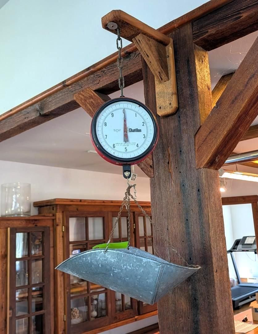 Hanging scale with a metal pan under a wooden beam inside a room