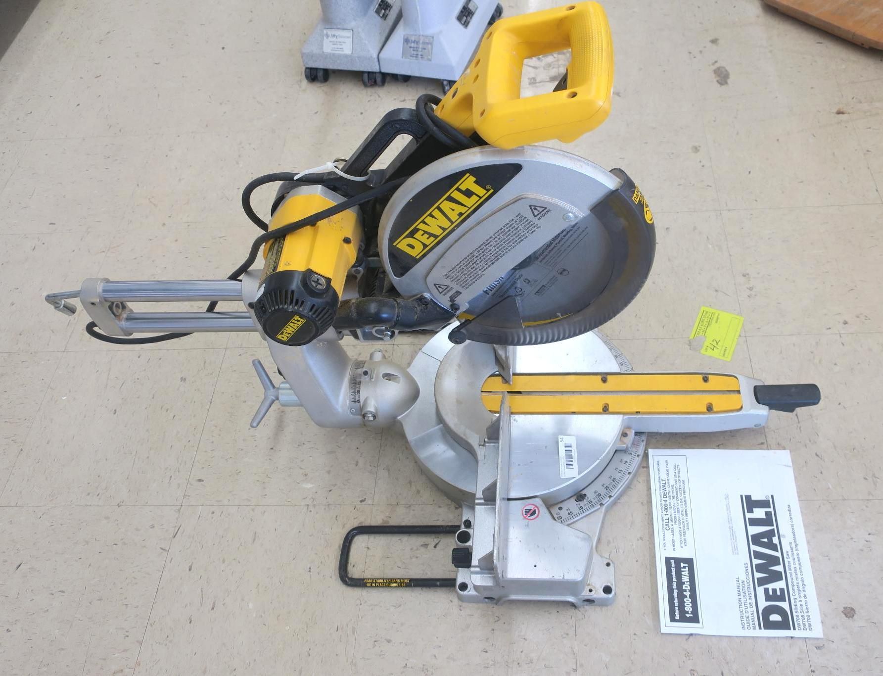Yellow and silver DeWalt miter saw on a concrete floor with attached blade guard and collection bag