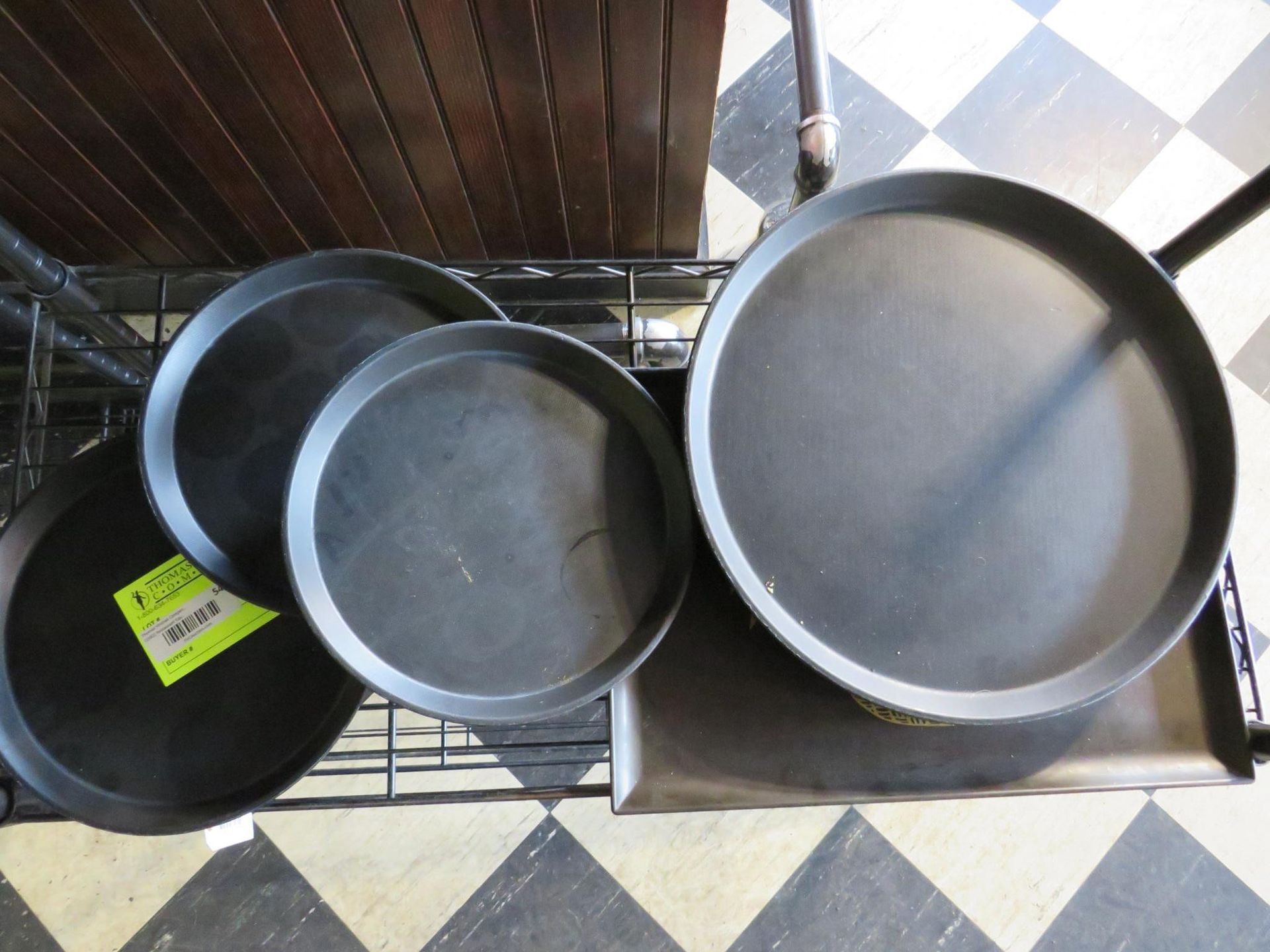 Four round, black metal pizza pans on a metal shelf.