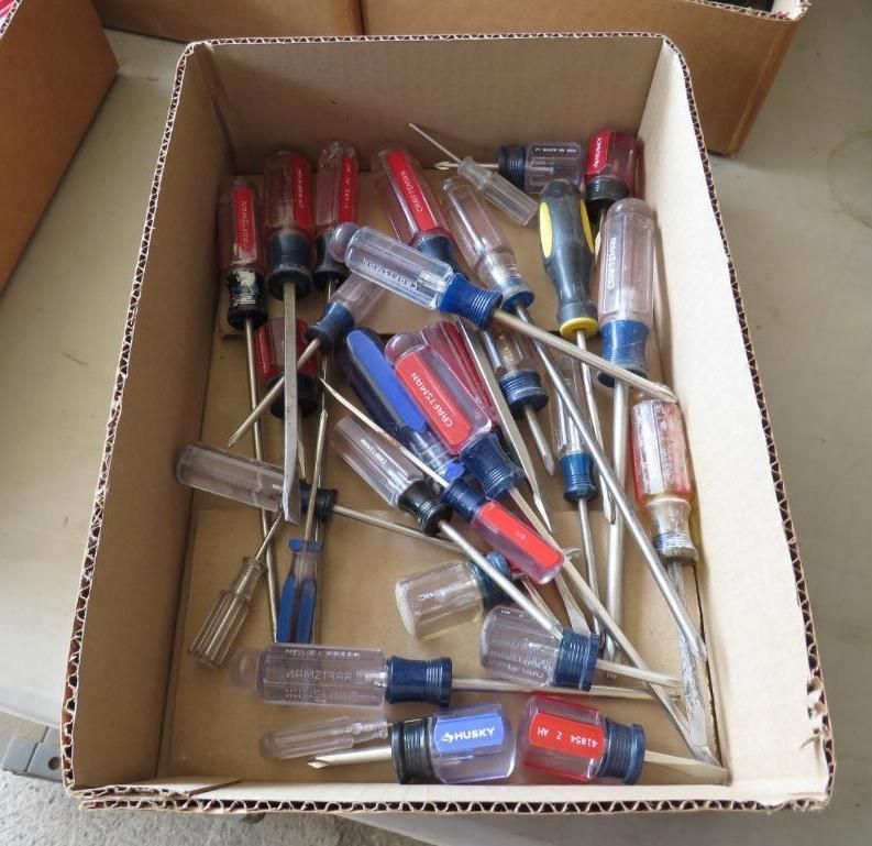 A cardboard box filled with various screwdrivers; mostly red and blue handles.