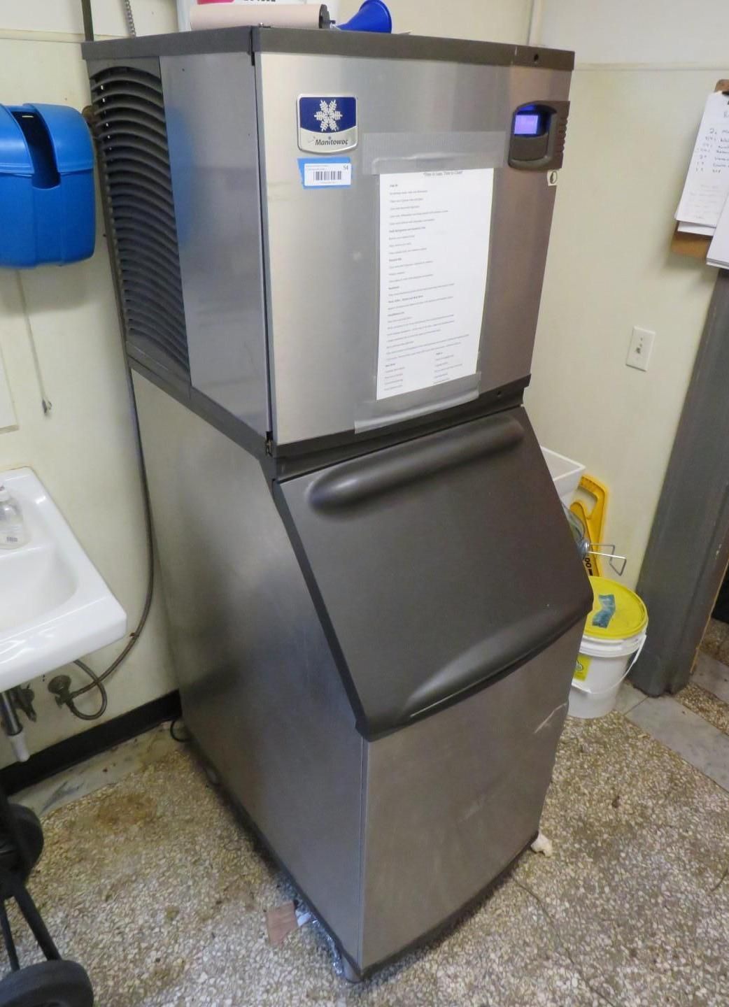 Stainless steel ice machine in a commercial setting, with a large bin door.