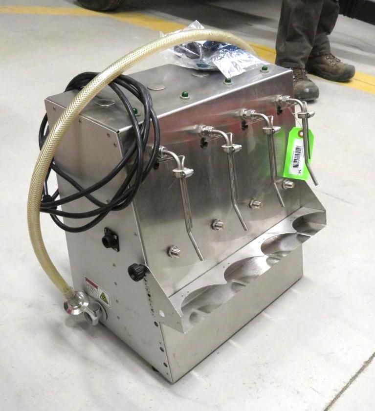 Stainless steel dispensing machine with four spouts, hose, and collection cups on a concrete floor.