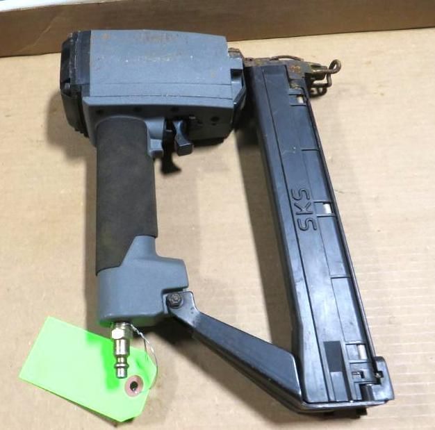 Pneumatic nail gun with a black and gray body, a green tag, and air hose fitting.