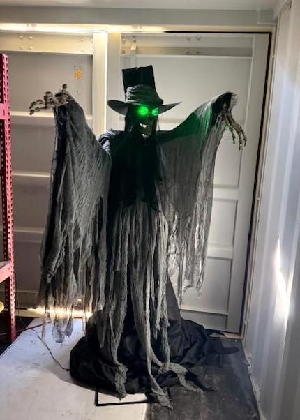Animated Halloween figure, black top hat and tattered cape, with glowing green eyes and outstretched arms. Indoors.