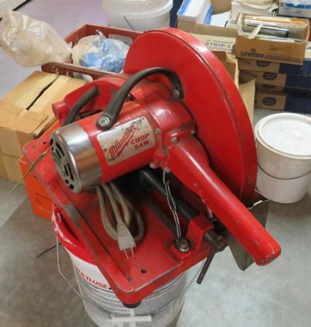 Red Milwaukee chop saw on a white bucket, indoors.