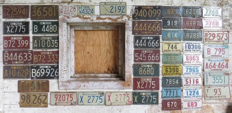 Collection of vintage license plates on a white wall.