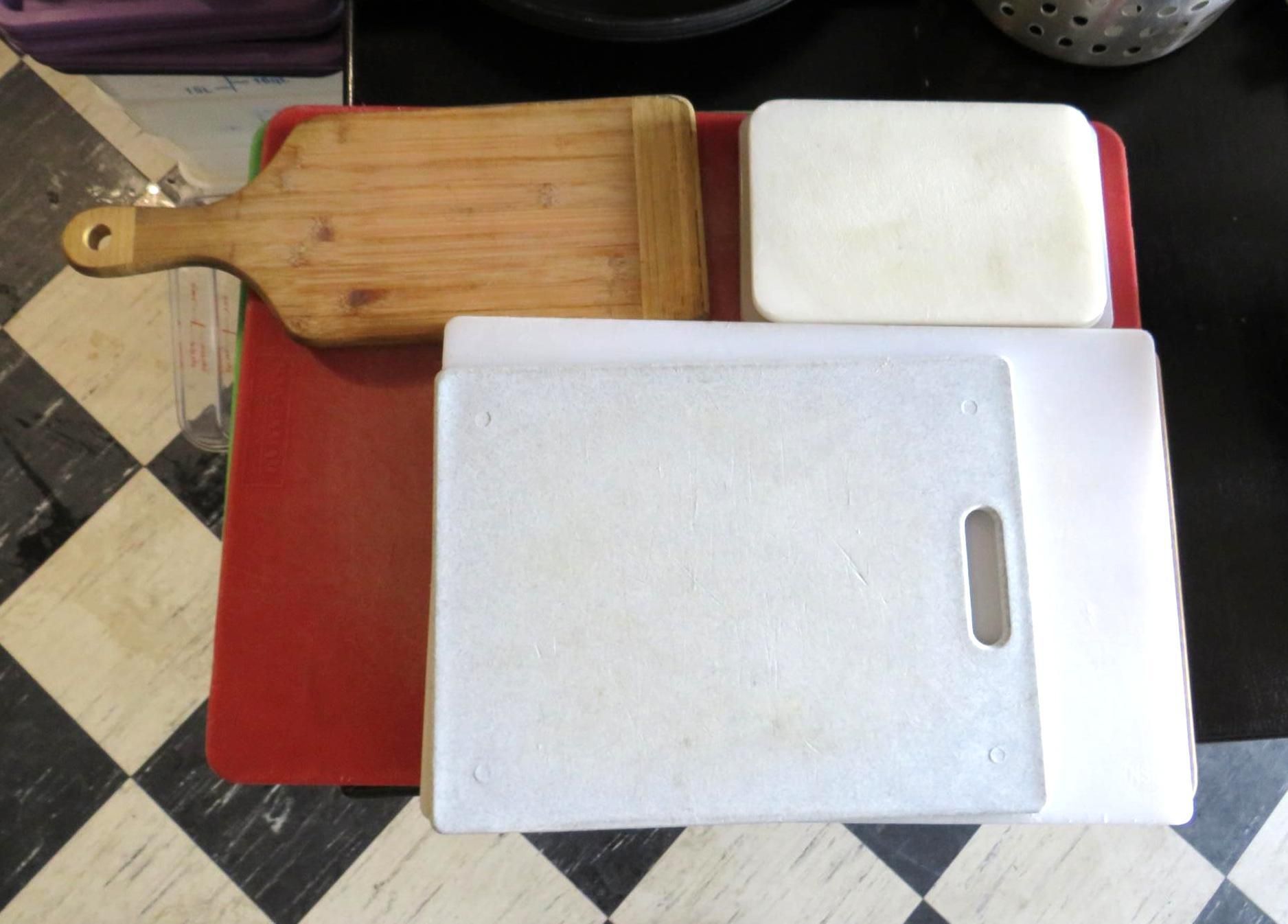Several cutting boards of various sizes and colors on a tiled surface.