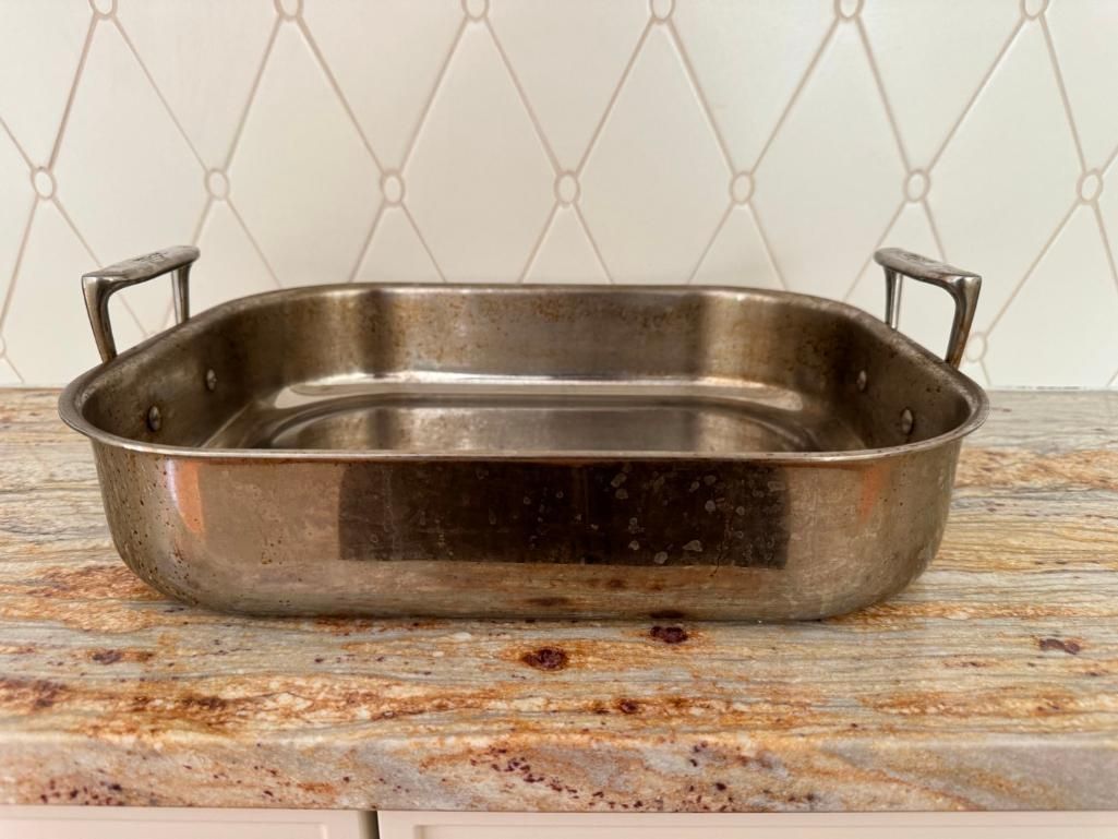 Stainless steel roasting pan with handles on a granite countertop.