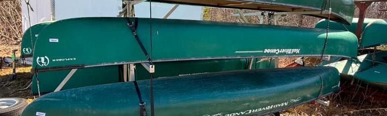 Green canoes stacked on a rack, some are labeled, outdoors.