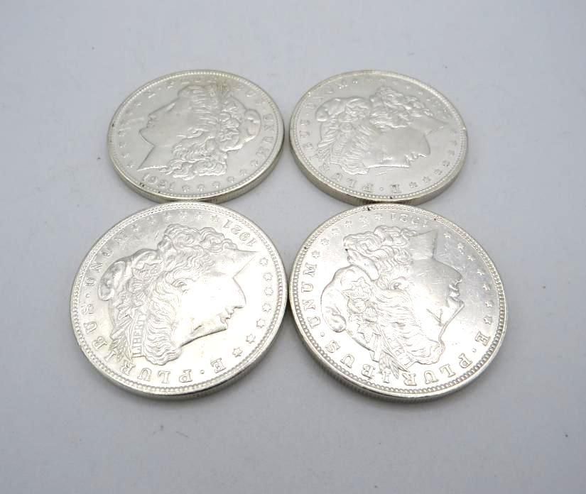Four silver Morgan dollar coins on a white background, each with a woman's profile.
