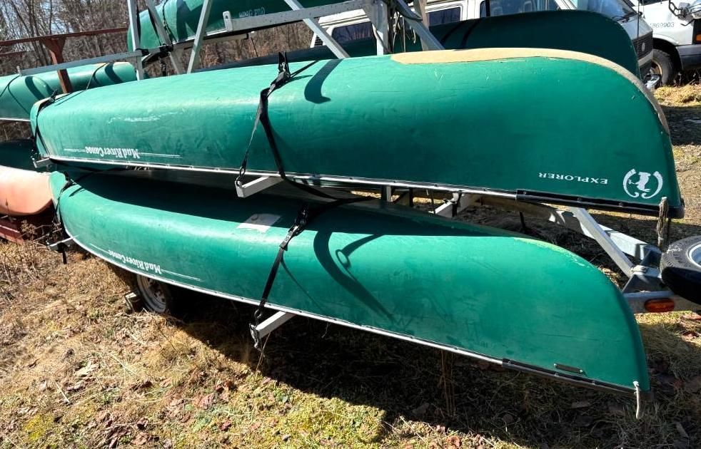 Two green canoes stacked on a trailer in an outdoor setting.
