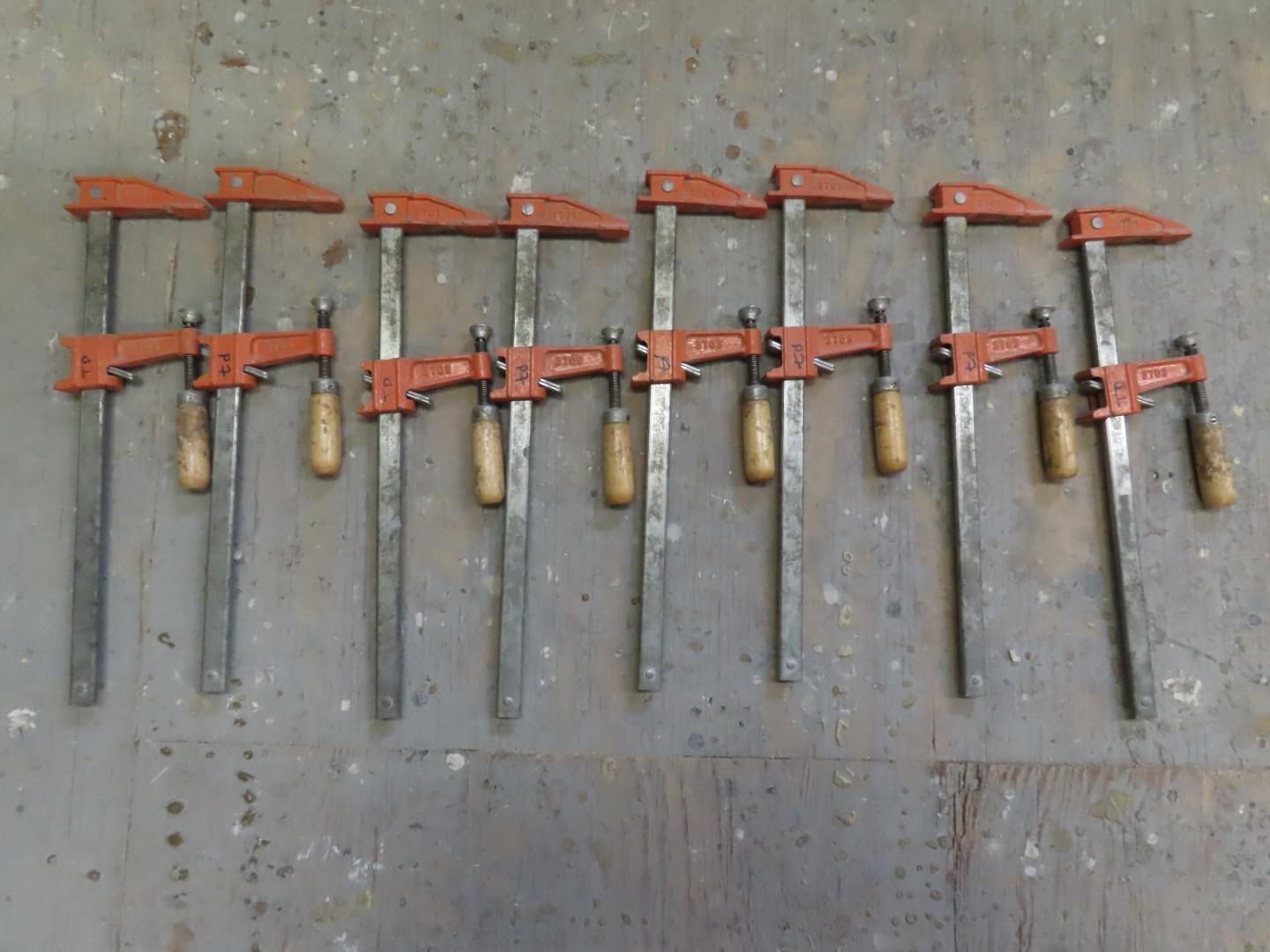 Eight orange pipe clamps lined up on a gray floor.