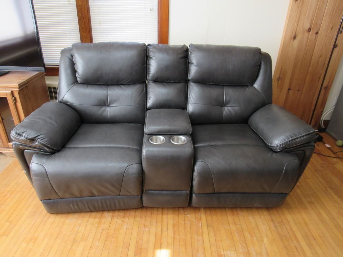 Gray leather reclining loveseat with center console, two cupholders, on wood floor.