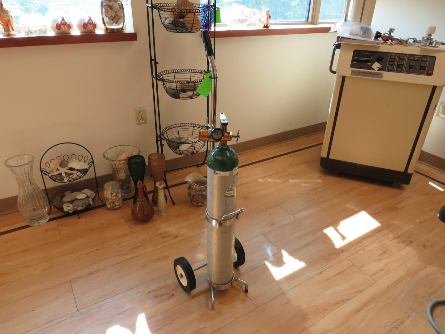 Oxygen tank on wheels in a room with hardwood floors and a shelf unit.