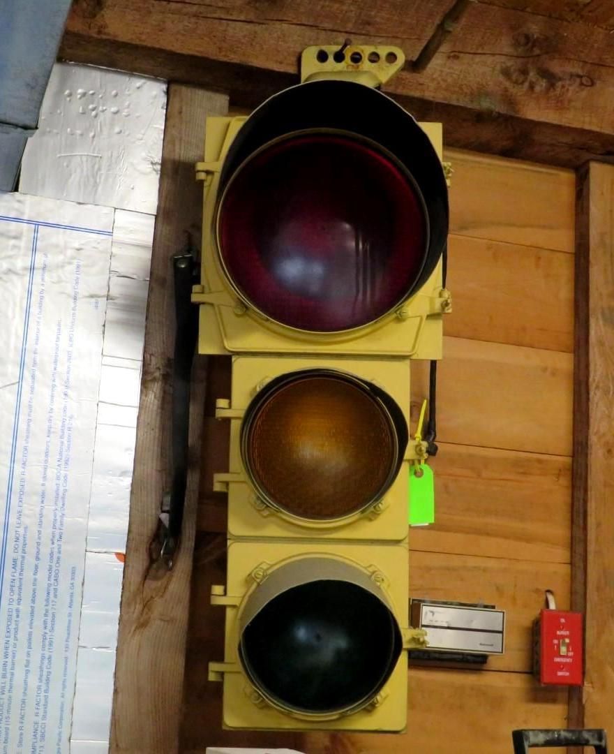 Yellow traffic light with red, yellow, and green lenses, mounted on a wooden wall.