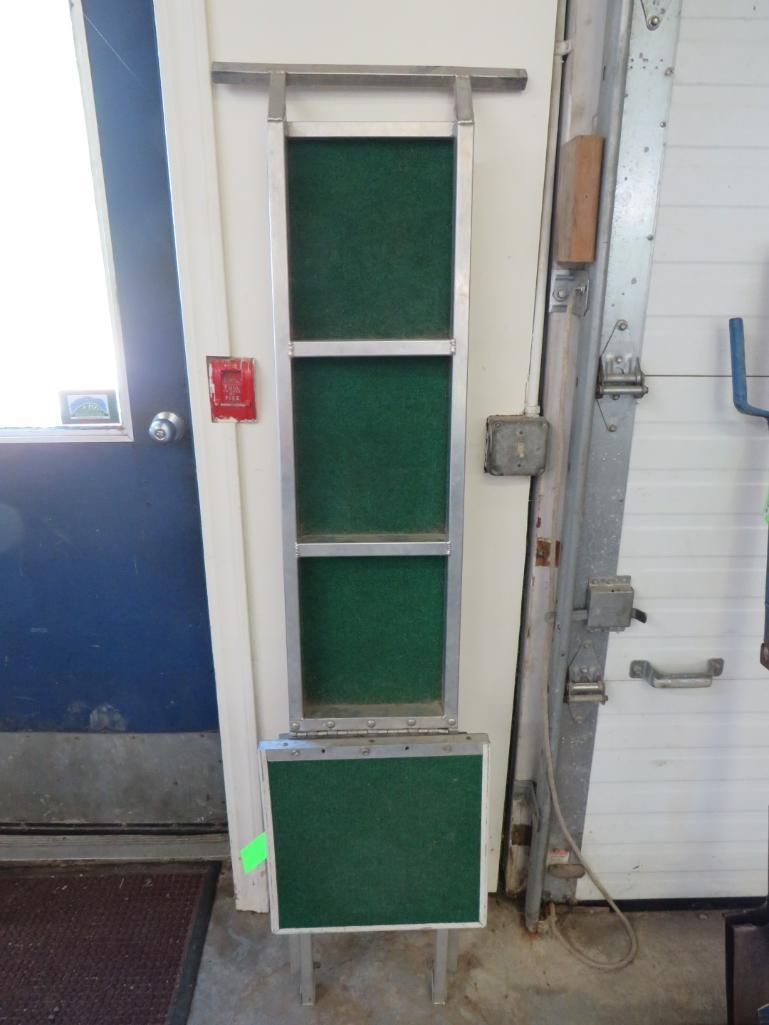 Green-carpeted shoe cleaning device mounted on a white wall, next to a blue door.