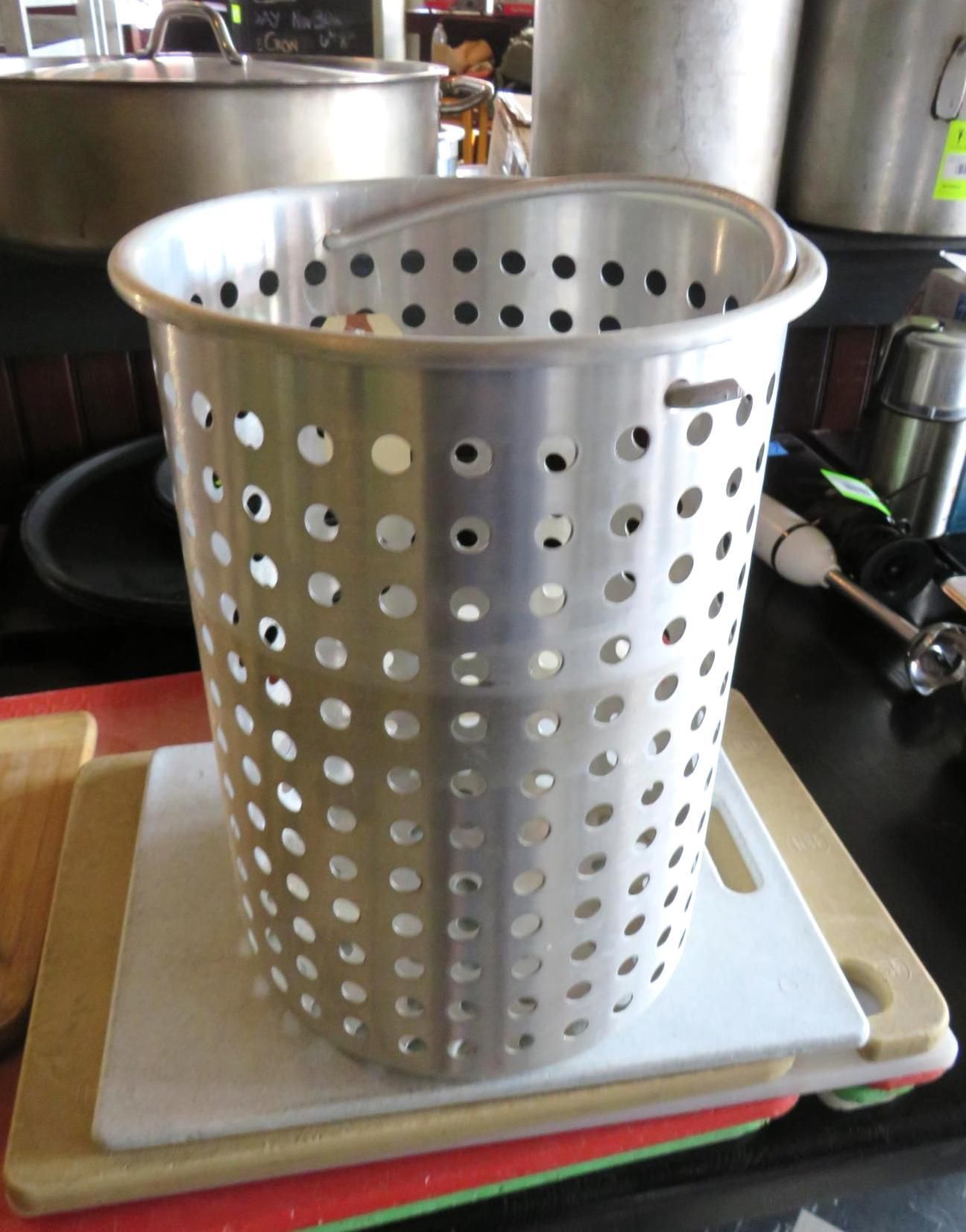 Metal perforated pot with handle on cutting boards.