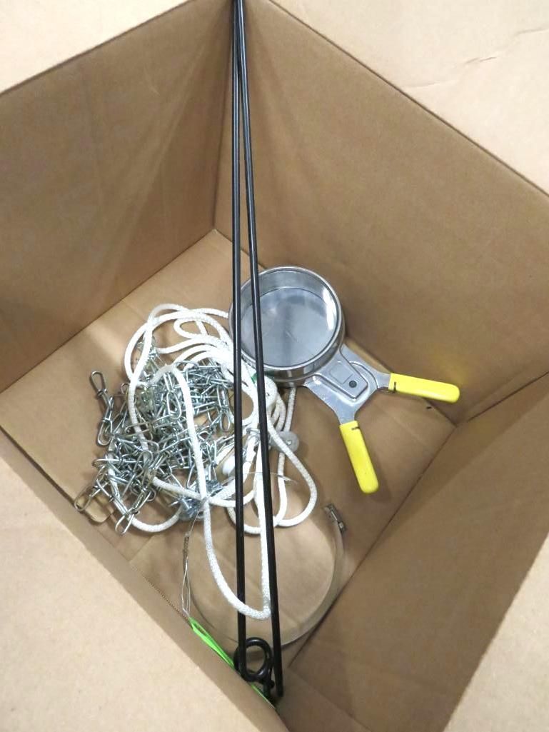 Cardboard box containing a metal clamp, rope, chain, and two black metal poles.