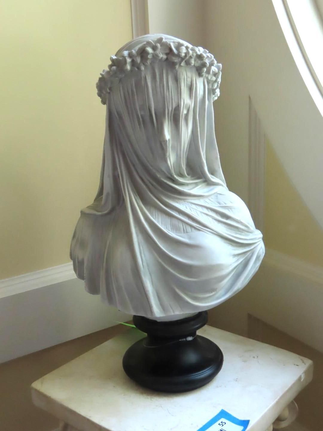 Marble bust of a veiled woman with floral crown, on black pedestal, displayed indoors.