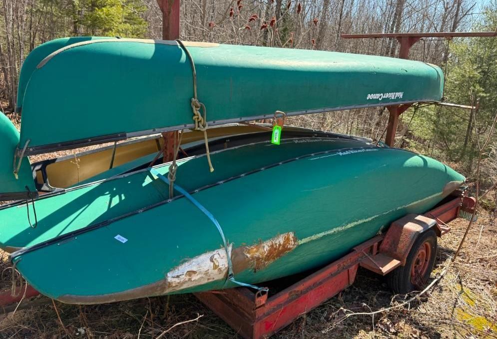 Two green canoes on a red trailer with a storage rack, outdoors.