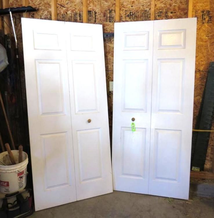 Two white bi-fold closet doors leaning against a wall in a garage.