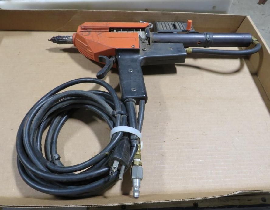 Orange and black industrial tool with attached air hose and power cord, lying on cardboard.
