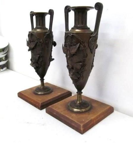 Two bronze urns with handles on wooden bases.