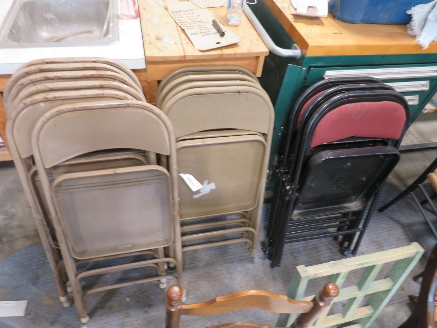 Stacks of folded metal chairs in varying colors, tan and black, near a wooden table.