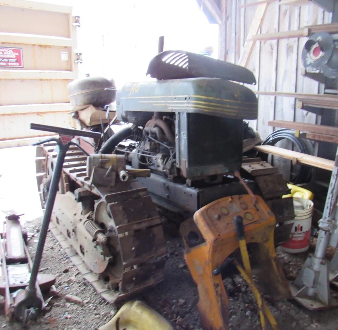 Old, green and yellow Caterpillar track-type tractor, parked indoors in a shed.