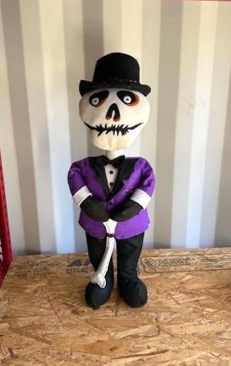 Skeleton figure wearing a purple suit and black hat, holding a cane, standing.